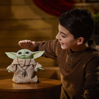 A child interacts with a Hasbro Star Wars The Mandalorian Animatronic The Child figure wearing a silver pendant.