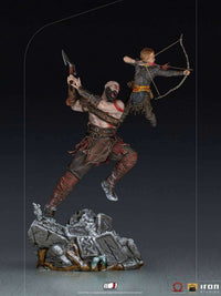 Iron Studios 1/10 Kratos and Atreus statue showing Kratos swinging an axe while Atreus aims a bow on a rocky base.