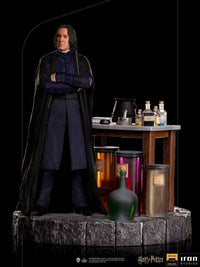 Iron Studios 1/10 Severus Snape statue standing with arms crossed beside a potion-filled wooden table on a stone base.