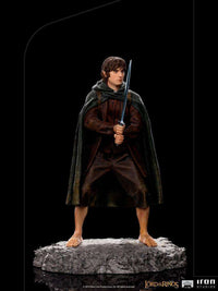 Iron Studios 1/10 scale Frodo statue standing on a rocky base, holding a sword and wearing a dark green hooded cloak.