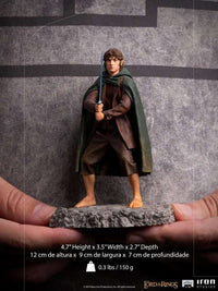 Front view of Iron Studios 1/10 Frodo statue holding Sting, featuring a green cloak and detailed rocky base.