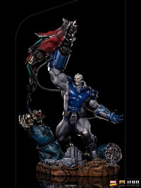Iron Studios 1/10 Apocalypse Deluxe statue in blue and grey armor, holding a robotic arm aloft on a rocky base.