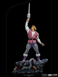 Iron Studios 1/10 Prince Adam statue holding the Power Sword aloft on a detailed rocky base, full-body side view.
