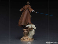Rear view of Iron Studios 1/10 Obi-Wan Kenobi statue featuring a brown Jedi robe, blue lightsaber, and rocky base.