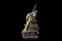 Iron Studios 1/10 scale Donatello statue in a dynamic pose, standing on a detailed industrial rooftop base.