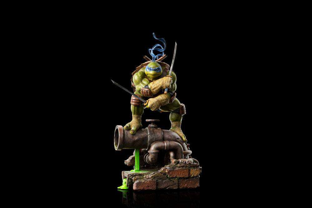 Iron Studios 1/10 Leonardo statue in a dynamic pose with katanas, standing on a sewer pipe base against a black background.