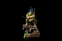 Iron Studios 1/10 Leonardo statue in a dynamic pose with katanas, standing on a sewer pipe base against a black background.