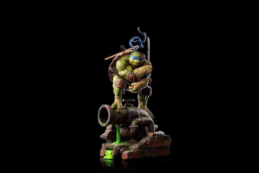 Iron Studios Leonardo 1/10 scale statue in a dynamic pose standing on a sewer pipe with green ooze on a black background.