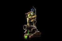 Iron Studios Leonardo 1/10 scale statue in a dynamic pose standing on a sewer pipe with green ooze on a black background.