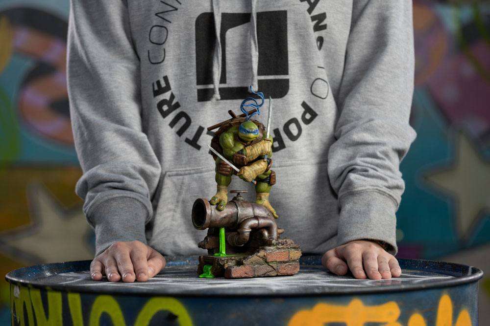 Iron Studios 1/10 scale Leonardo statue standing on a sewer pipe base, held by a person in a grey hoodie.