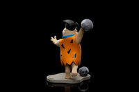 Side view of Iron Studios Fred Flintstone 17cm statue wearing his iconic orange tunic while bowling on a stone base.
