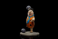 Iron Studios 1/10 scale Fred Flintstone statue in an orange tunic and blue tie, posed with a bowling ball on a base.