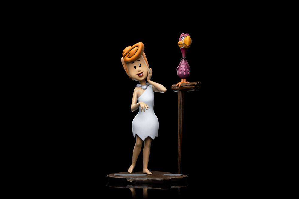 Iron Studios 1/10 Wilma Flintstone statue in a white dress standing next to a small purple bird on a wooden perch.