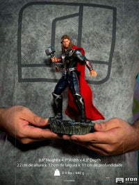 Hands holding an Iron Studios 1/10 Thor Battle of NY statue featuring a detailed metallic suit and flowing red cape.