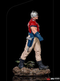 Side view of Iron Studios Peacemaker 1/10 scale statue wearing his iconic chrome helmet, red shirt, and tan pants.