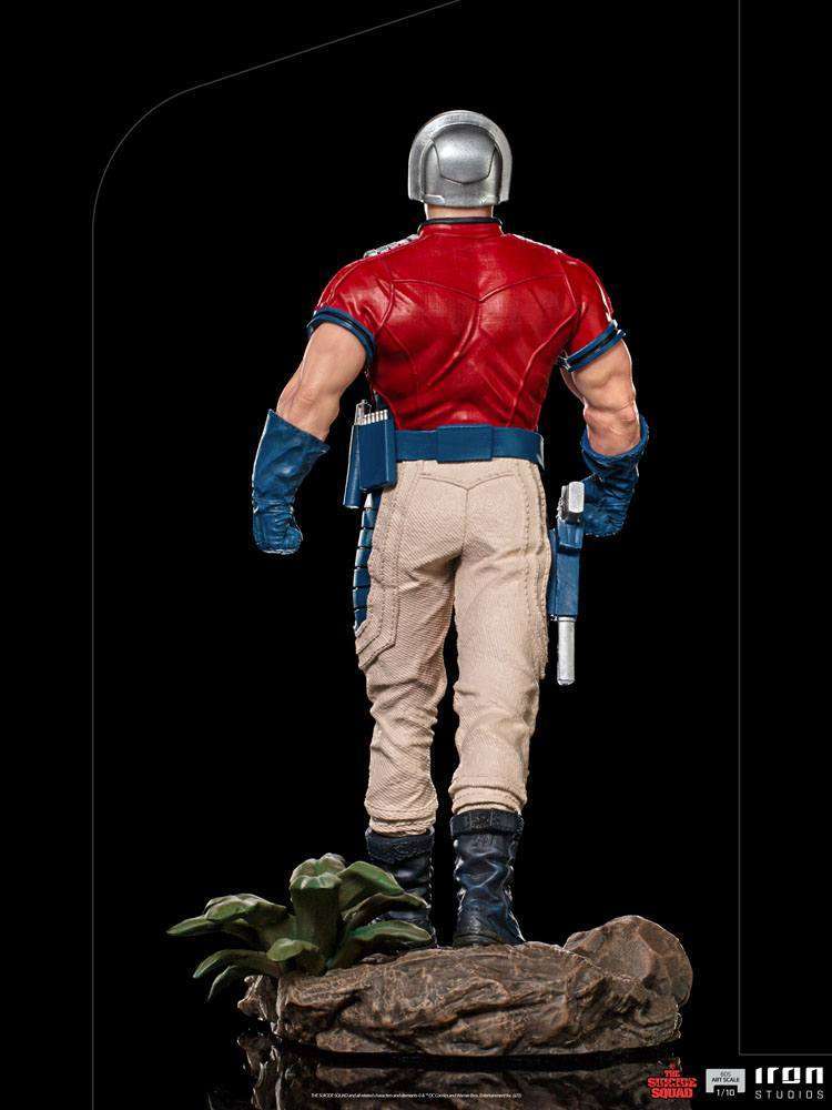 Back view of Iron Studios Peacemaker 1/10 scale statue in red shirt, beige pants, and chrome helmet on rocky base.