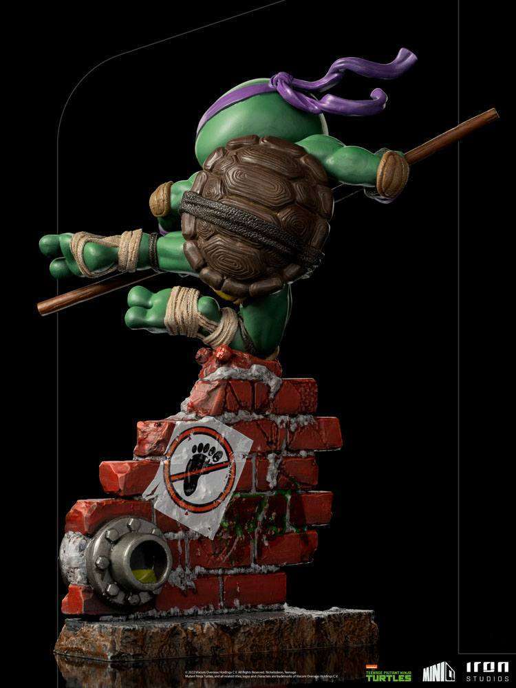 Back view of Iron Studios Donatello PVC figure, 21 cm, leaping over a brick wall base with a Foot Clan logo sticker.