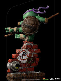 Back view of Iron Studios Donatello PVC figure, 21 cm, leaping over a brick wall base with a Foot Clan logo sticker.