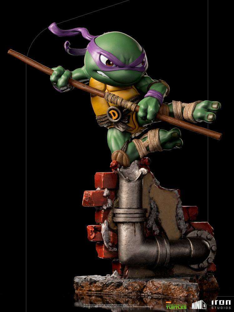 Iron Studios Donatello PVC figure in a dynamic pose with his bo staff, standing on a brick wall base, 21 cm tall.