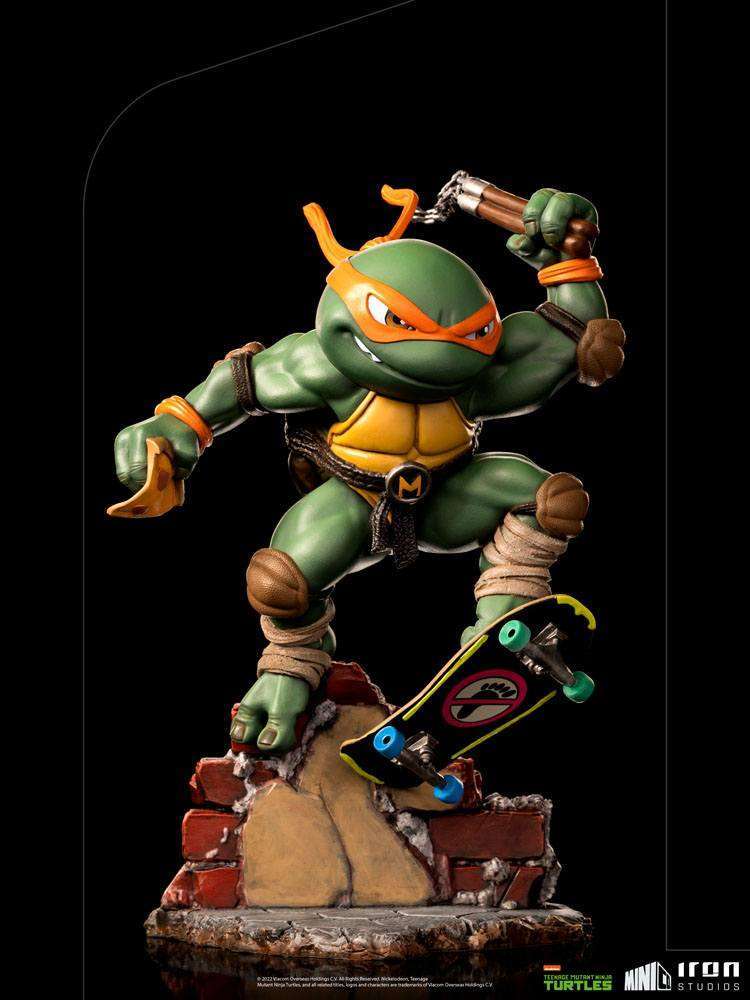 Iron Studios Michelangelo Mini Co. PVC figure in a dynamic pose on a skateboard over a brick base, front view.