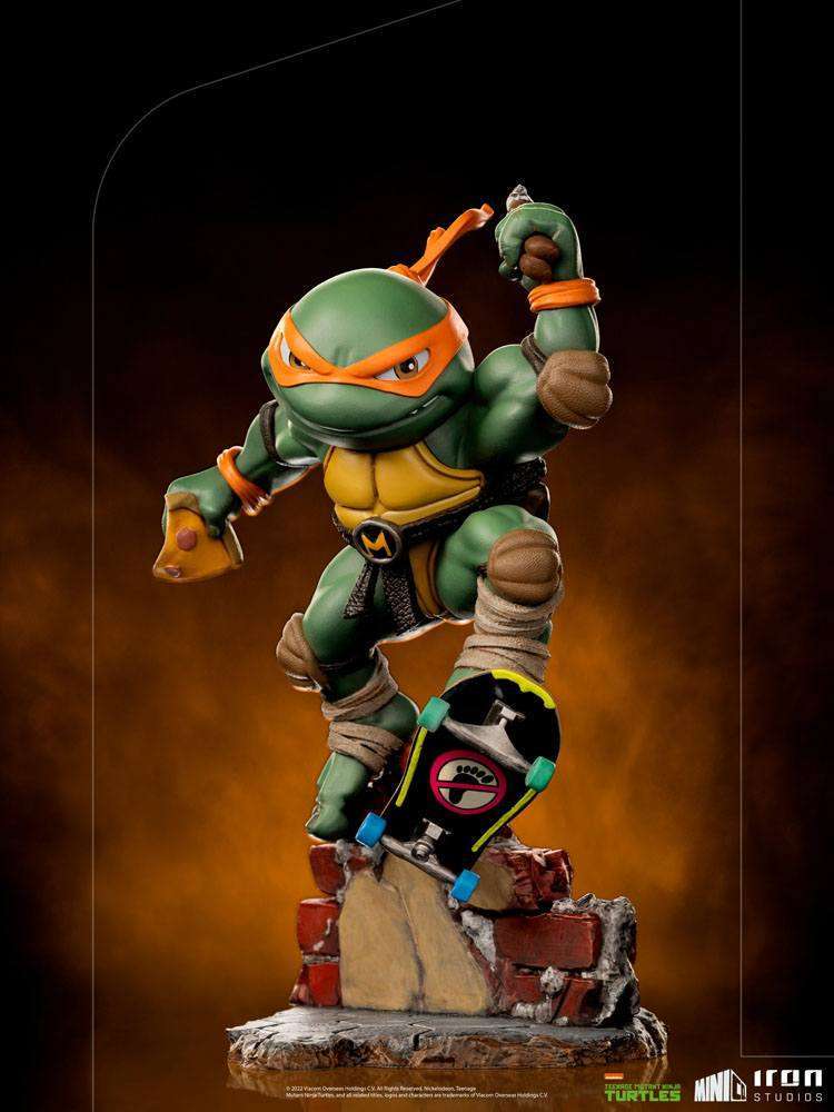 Iron Studios Michelangelo Mini Co. PVC figure in a dynamic pose on a skateboard over a brick base, front view.