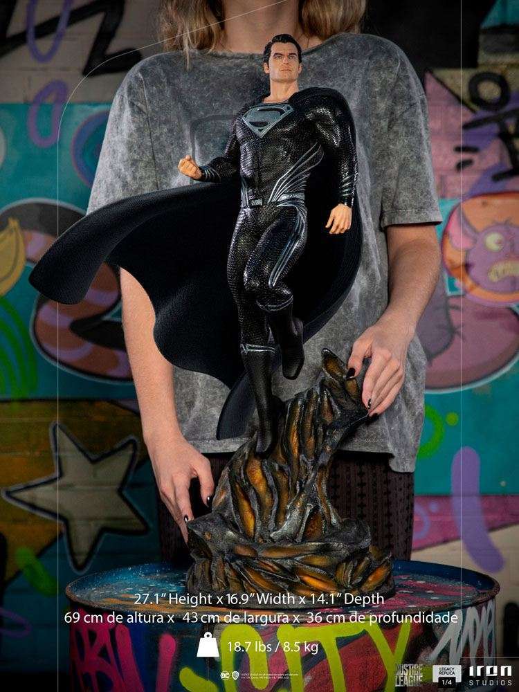Front view of Iron Studios 1/4 scale Superman Black Suit statue with flowing cape on a rocky base held by a person.